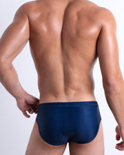 Back view of a model wearing CASINO ROYALE (BLUE) men’s beach brief in dark blue color. Inspired by actor Daniel Craig's iconic blue swim trunks worn in the 2006 film Casino Royale, is designed by BANG! Clothes in Miami.
