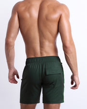 Back view of male model wearing men’s CASINO ROYALE (GREEN) beach Flex Boardshorts swimming shorts in a green color. Inspired by actor Daniel Craig's iconic blue swim trunks worn in the 2006 film Casino Royale, are designed by BANG! Clothes in Miami.