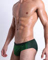 Side view of muscular male model wearing CASINO ROYALE (GREEN) Summer swim brief swimsuit for the beach with a stylish color block design in green for men. This high-quality brief is by BANG! Clothes, a men’s beachwear brand from Miami. Inspired by the iconic style of Daniel Craig's blue swim trunks in the 2006 film Casino Royale.