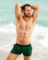 Male model relaxing on the beach, wearing CASINO ROYALE (GREEN) Show Shorts by BANG! Clothing. These lightweight, quick-dry swimming shorts offer a stylish, comfortable fit, perfect for beach lounging and water activities. Featuring a rich green color and sleek design.