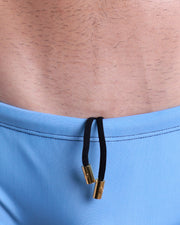 Close-up view of the CASINO ROYALE (BLUE) men’s drawstring swimsuit showing black cord with custom branded golden cord ends, and matching custom eyelet trims in gold.