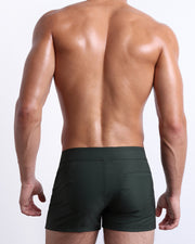 Back view of male model wearing men’s CASINO ROYALE (GREEN) beach Beach Shorts swimsuits in a blue color. Inspired by actor Daniel Craig's iconic blue swim trunks worn in the 2006 film Casino Royale, are designed by BANG! Clothes in Miami.