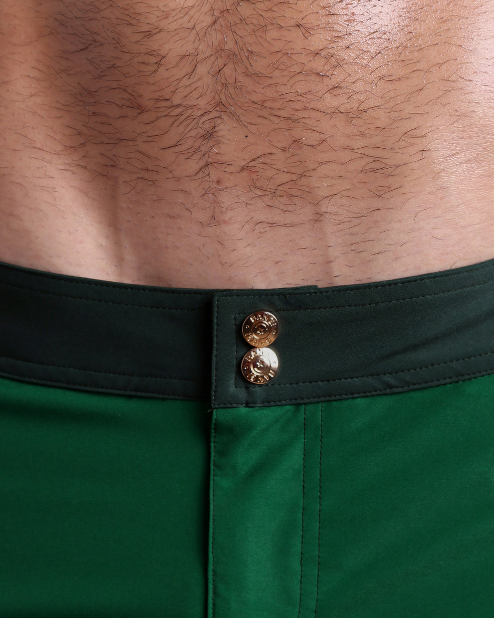 Close-up view of inseam and details of CASINO ROYALE (GREEN) swimsuit for men, showing custom branded golden buttons.