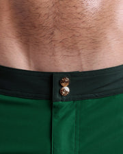 Close-up view of inseam and details of CASINO ROYALE (GREEN) swimsuit for men, showing custom branded golden buttons.