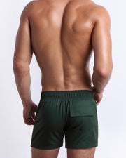 Back view of male model wearing men’s CASINO ROYALE (GREEN) beach Flex Shorts swimsuits in a green color. Inspired by actor Daniel Craig's iconic blue swim trunks worn in the 2006 film Casino Royale, are designed by BANG! Clothes in Miami.
