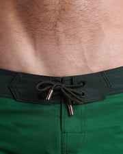 Close-up view of men’s summer Flex shorts by BANG! clothing brand, showing green color cord with custom-branded golden cord ends, and matching custom eyelet trims in gold.