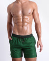 Male model wearing CASINO ROYALE (GREEN), premium swimwear with a stylish color block design in dark green and light green for men. These high-quality swimwear bottoms by BANG! Clothes, a men’s beachwear brand from Miami, is inspired by the iconic style of Daniel Craig's blue swim trunks in the 2006 film Casino Royale.