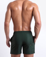 Back view of male model wearing men’s CASINO ROYALE (GREEN) beach Resort Shorts swimsuits in a blue color. Inspired by actor Daniel Craig's iconic blue swim trunks worn in the 2006 film Casino Royale, are designed by BANG! Clothes in Miami.