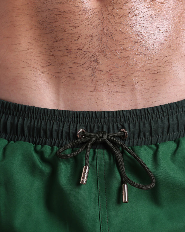 Close-up view of inseam and details of CASINO ROYALE (GREEN) swimsuit for men, with dark green cord and custom branded golden cord-ends, and matching custom eyelet trims in gold. 
