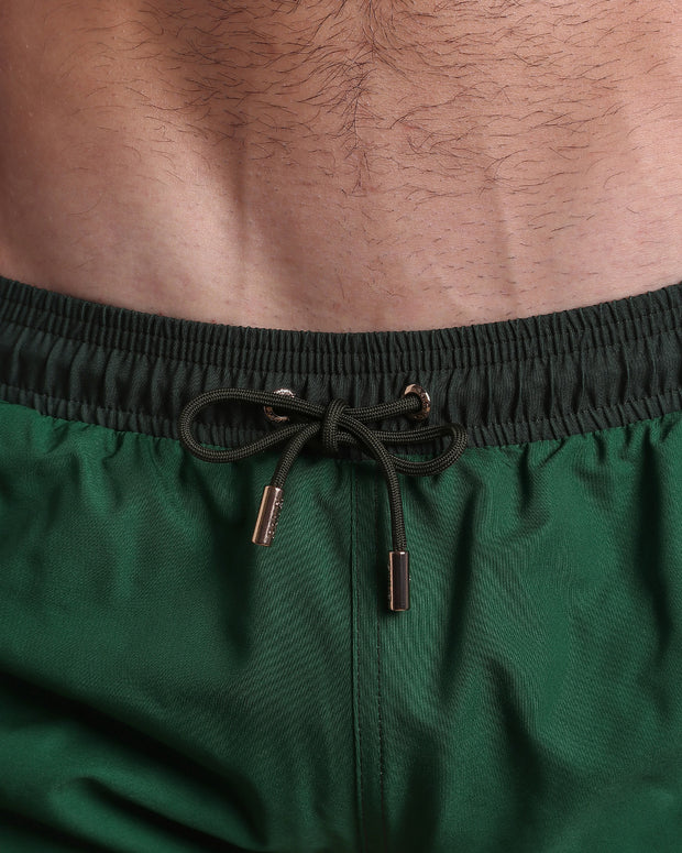 Close-up view of the CASINO ROYALE (GREEN) men’s summer shorts, showing light blue cord with custom branded golden cord ends, and matching custom eyelet trims in gold.