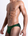 Side view of muscular male model wearing CASINO ROYALE (GREEN) Summer swim brief swimsuit for the beach with a stylish color block design in green for men. This high-quality brief is by BANG! Clothes, a men’s beachwear brand from Miami. Inspired by the iconic style of Daniel Craig's blue swim trunks in the 2006 film Casino Royale.