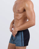 Side profile of a male model wearing the CASINO ROYALE (GREY) Show Shorts by BANG! These fitted swim shorts showcase deep slip pockets with waterproof zippers, a quad-friendly short leg cut, and a contoured fit that enhances movement and style.