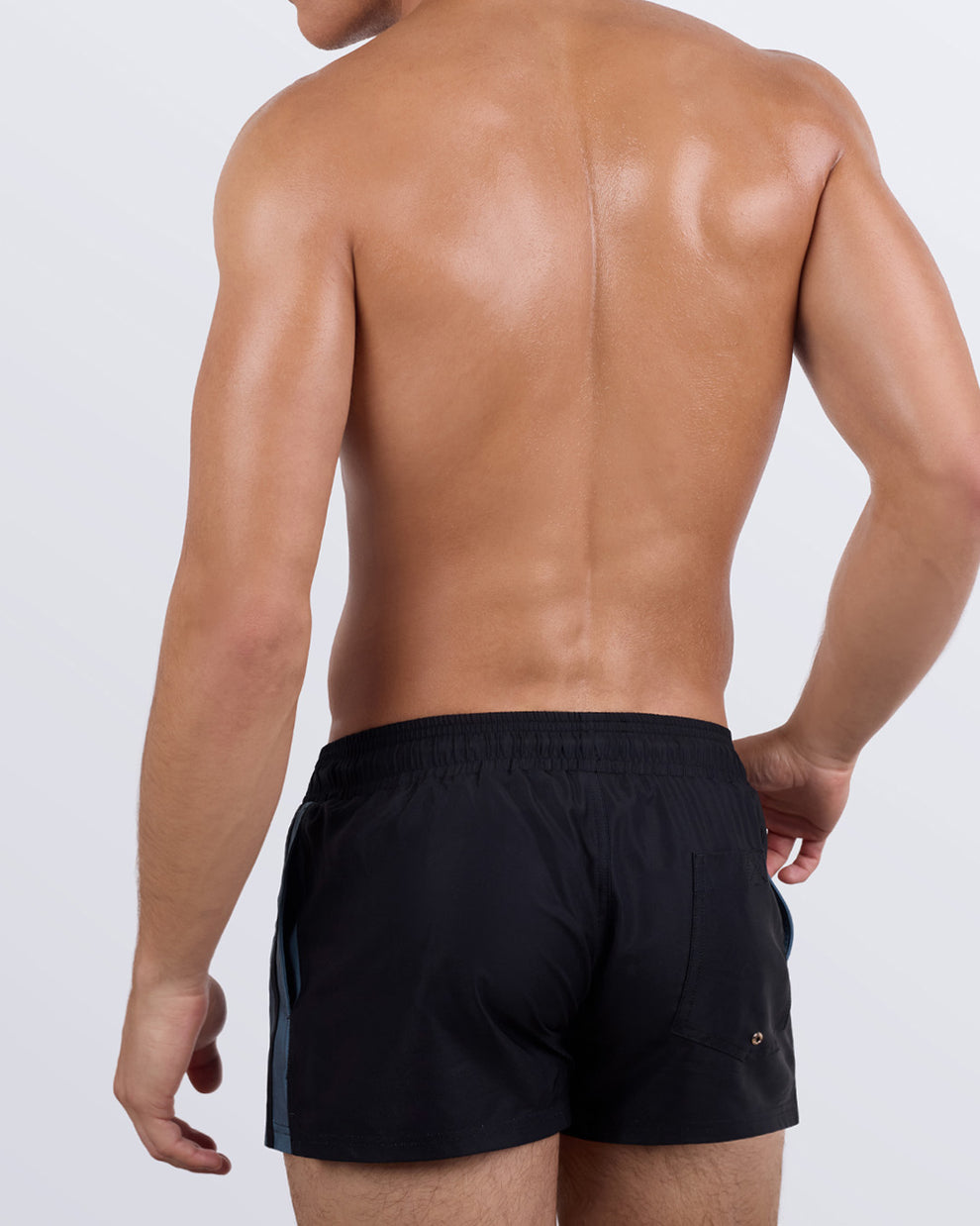Rear view of a male model in the CASINO ROYALE (GREY) Show Shorts by BANG! The shorts feature a solid black back panel, an elasticated waistband for a secure fit, a functional back pocket with a discreet snap closure, and a lightweight, quick-drying fabric.