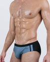 Front angled view of BANG! Casino Royale (Grey) Swim Briefs – men's low-rise swimwear in slate grey with black side panels and logo detail.