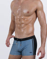 Angled front view of the CASINO ROYALE Swim Trunks in Grey – steel blue-grey tone with black waistband and side panel, finished with gold-tipped drawstring.