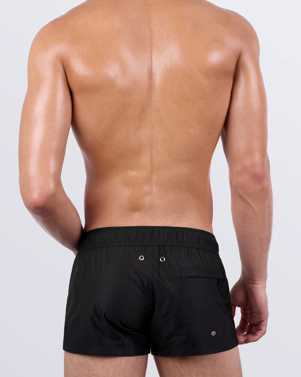 Back view of a male model in the Casino Royale (Leopard + Black) Mini Shorts by BANG! Miami. These stylish men’s swim shorts showcase a solid black back panel, a functional back pocket with metallic drainage grommets, and a quick-dry fabric that enhances comfort and performance.
