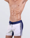 Side view close-up of a male model in the Casino Royale (White + Navy Blue) Flex Shorts for men by BANG! Miami. The premium four-way stretch fabric, hybrid waistband, and deep zippered pockets enhance both style and functionality, perfect for versatile wear from beach to city.