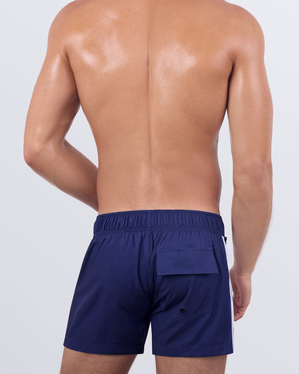 Back view of a male model wearing the Casino Royale (White + Navy Blue) Flex Shorts by BANG! Miami. The sophisticated swim shorts showcase a functional flap pocket with a secure closure, deep zippered side pockets, quick-dry fabric, and a structured fit that complements the athletic silhouette.