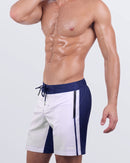Close-up side view of a male model in the CASINO ROYALE (WHITE + NAVY BLUE) - Flex Boardshorts by BANG! Miami. The design includes deep zippered pockets for secure storage, premium metal-tipped drawstrings, and a streamlined silhouette for a sleek, athletic look.