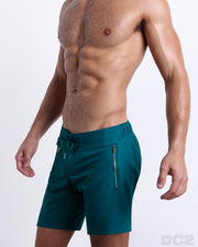 Side view of the CHIC TEAL for men’s summer long boardshorts with dual zippered pockets in a solid vibrant teal green color designed by DC2 a brand based in Miami.
