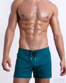Male model wearing CHIC TEAL beach Flex Shorts, premium swimwear in a solide green teal color for men. These high-quality swimwear bottoms by DC2, a men’s beachwear brand from Miami.