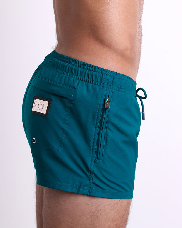 Side view of the CHIC TEAL swimsuit Poolside Shorts men’s shorter length shorts with side zipper pocket featuring a bright teal green color. These high-quality swimwear bottoms by DC2, a men’s beachwear brand from Miami.