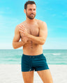 Model on the beach wearing CHIC TEAL Poolside Shorts by DC2 Miami. These relaxed-fit men's swim shorts combine comfort and style for sunny beach outings.