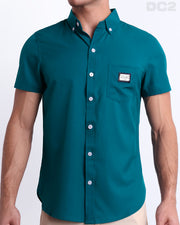 This is a front view of a male model looking sexy in a CHIC TEAL stretch shirt for men. The shirt is a vibrant teal color on the left pocket. It's a premium quality button-up top made by DC2, a Miami-based men's beachwear brand.This is a front view of a male model looking sexy in a CHIC TEAL Stretch Shirt and a the NAKED PINK Beach Shorts for men.