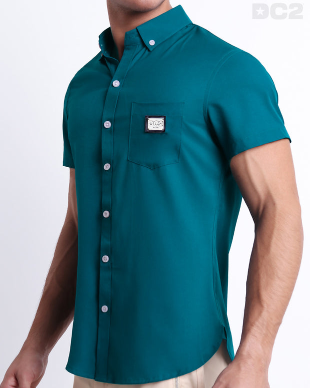 Side view of a masculine model wearing the men’s CHIC TEAL Summer button-down shirt in a solid blue/green color. This high-quality shirt is by DC2, a men’s beachwear brand from Miami.