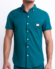 This is a front view of a male model looking sexy in a CHIC TEAL stretch shirt for men. The shirt is a vibrant teal color on the left pocket. It's a premium quality button-up top made by DC2, a Miami-based men's beachwear brand.