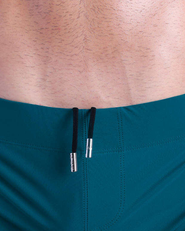 Close-up view of men’s summer beach shorts by DC2 clothing brand, showing black cord with custom branded metallic silver cord ends.