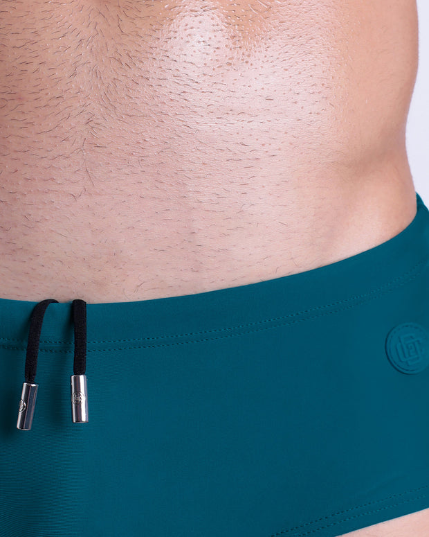Close-up view of the CHIC TEAL men’s drawstring briefs showing black cord with custom branded metallic silver cord ends, and matching custom eyelet trims in silver.