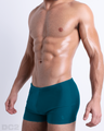 Side view of a masculine model wearing men’s swimsuit compression shorts in a blue green teal color featuring a side pocket with official logo of DC2 Brand.