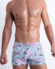 Male model wearing CLOSE TO YOU Beach Shorts, men’s Summer shorts with dual zippered pockets. Inspired by exotic birds on top of branches and pink flowers. These high-quality swimwear bottoms by DC2, a men’s beachwear brand from Miami.
