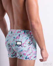 "Side view of the CLOSE TO YOU men’s summer Beach Shorts, with dual zippered pockets. The shorts have a stylish exotic birds design in a light blue color with pink flowers for men. These high-quality swimwear bottoms by DC2, a men’s beachwear brand from Miami. "