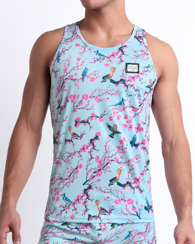 Male model wearing CLOSE TO YOU men’s casual Tank Top and the matching beach shorts. A premium quality swim set in a stylish exotic birds design in a light blue color with pink flowers, a men’s beachwear brand from Miami.