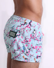 Side view of the CLOSE TO YOU men’s summer Poolside Shorts, with dual zippered pockets. The shorts have a stylish exotic birds design in a light blue color with pink flowers for men. These high-quality swimwear bottoms by DC2, a men’s beachwear brand from Miami.
