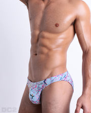 Side view of muscular male model wearing CLOSE TO YOU Summer Swim Mini Brief. This swimsuit Inspired by exotic birds on top of branches and pink flowers, designed by DC2 in Miami.
