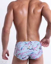 Back view of male model wearing the CLOSE TO YOU beach sexy Brazilian Sunga for men in a light blue color with an exotic birds print, designed by DC2.