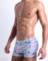 Side view of muscular male model wearing CLOSE TO YOU Summer swimming Trunks. This swimsuit Inspired by exotic birds on top of branches and pink flowers, designed by DC2 in Miami.