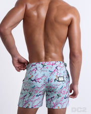 Back view of male model wearing men’s CLOSE TO YOU beach Tailored Shorts swimsuits in a light blue color with an exotic birds print, complete with a back pocket, designed by DC2. 