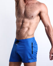 Side view of CLUB BLUE men’s shorter length shorts in cobalt blue color with side zipper pockets made by Miami-based Bang Clothing of men's beachwear