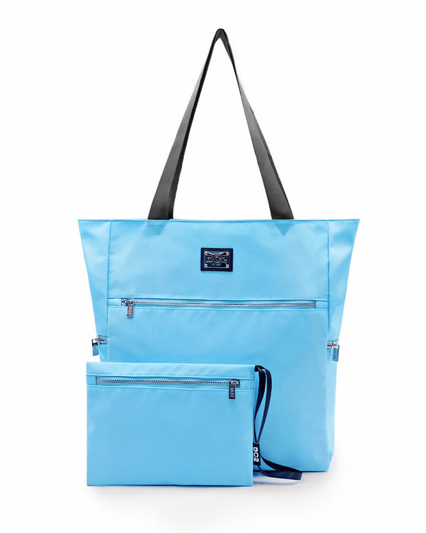 Front view of the COSTAL BLUE Poolside Tote Bag by DC2 Miami, featuring a sleek solid light sky blue color. The tote is spacious with durable black handles and multiple zippered compartments, including a detachable pouch with a matching color. Made from high-quality, water-resistant material, this versatile tote bag is perfect for beach outings or casual everyday use.