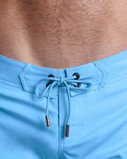 Close-up view of inseam and details of COASTAL BLUE shorts for men, with a sky blue color cord and custom branded silver cord-ends, and matching custom eyelet trims in black. 