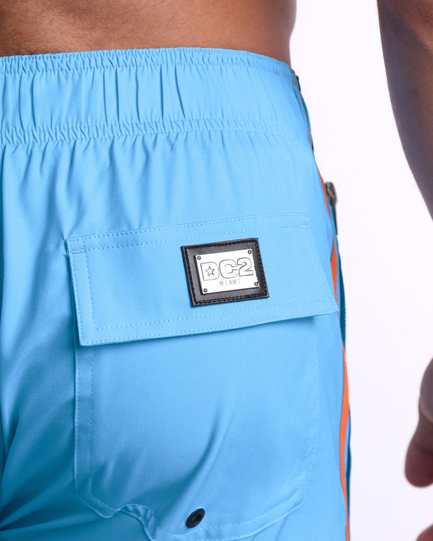 Close-up view of the COASTAL BLUE men’s Flex Boardshorts back pocket, showing custom branded silver metal logo.