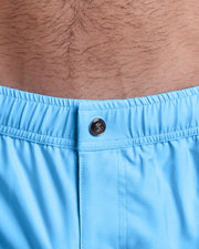Close-up view of the COASTAL BLUE men’s swimwear, showing custom branded silver metal logo.