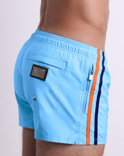 Side view of the COASTAL BLUE for men’s summer Poolside Shorts with dual zippered pockets. The shorts are in a solid light blue color with side navy and orange stripes for men made by DC2 a brand based in Miami.