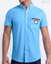 Male model wearing COASTAL BLUE men’s sleeveless stretch shirt. A premium quality top in a solid light blue color with orange and navy blue stripes on the pocket, a men’s beachwear brand from Miami.