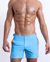 Male model wearing COASTAL BLUE Tailored Shorts, solid light blue color with orange and navy blue stripes on the side for men. These premium quality swimwear bottoms are DC2 by BANG! Clothes, a men’s beachwear brand from Miami.