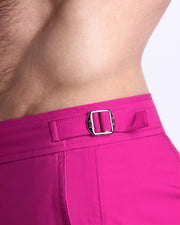 Close-up view of the CONFESS MAGENTA men’s swimwear, showing custom branded golden adjustable side buckles.